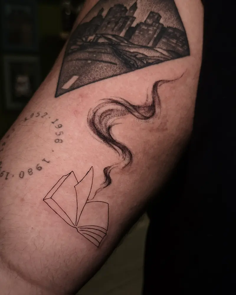 Tattoo work: a mountain landscape with an open book and a curl of smoke, on a thigh