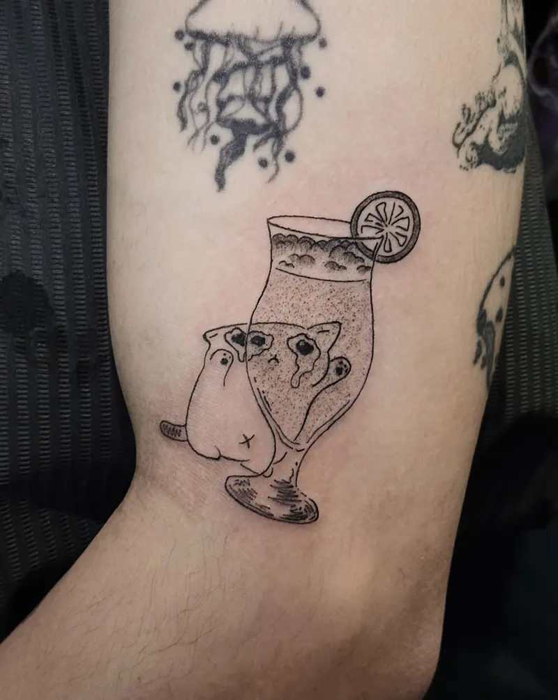 Tattoo work: a duck floating in a cocktail glass with a slice of lemon, on an inner arm