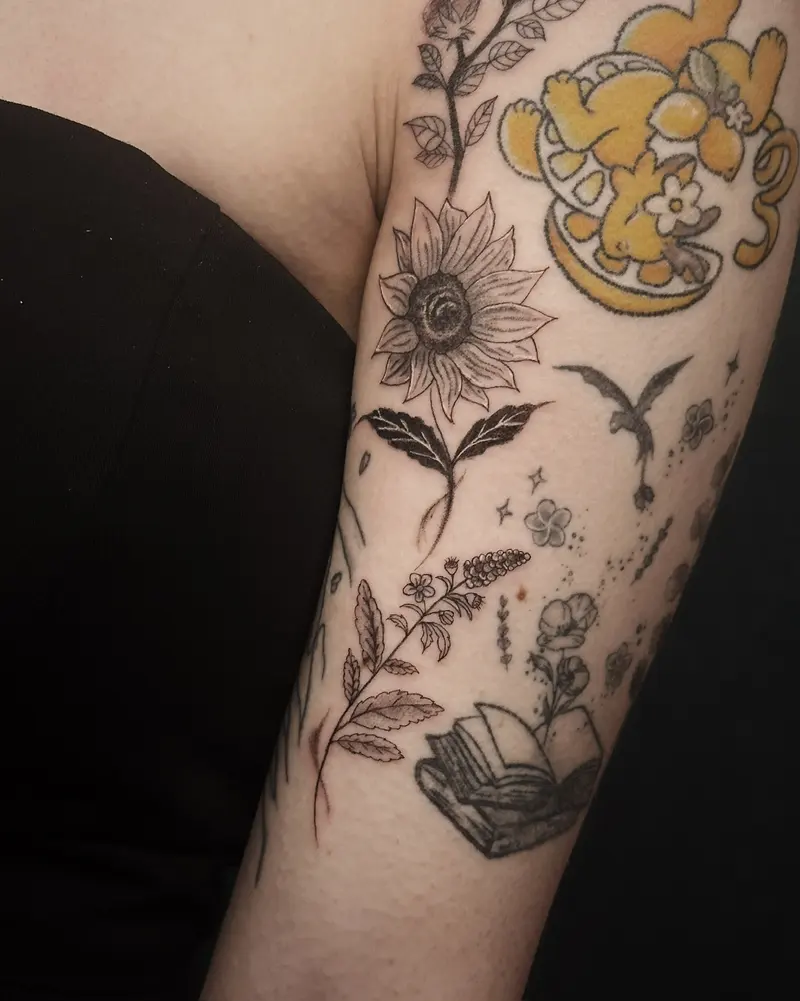 Tattoo work: sunflowers and botanicals beside a small colour character, on an upper arm