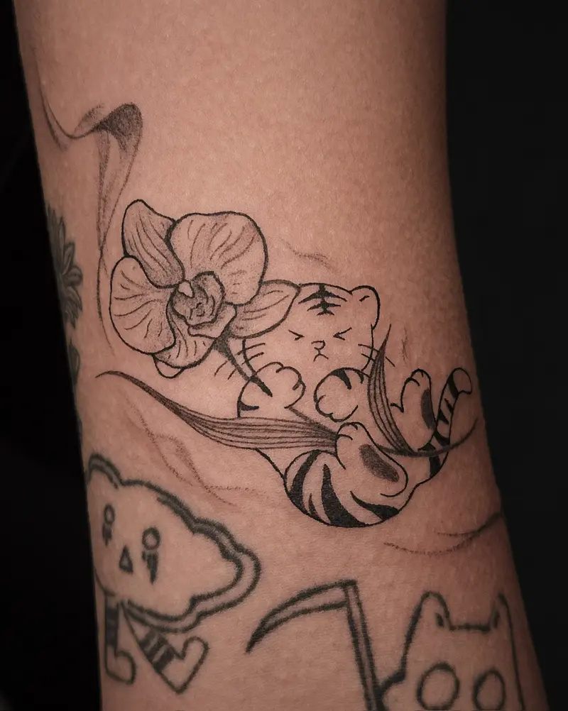 Tattoo work: an orchid with a cat and a cloud, touched with colour, on an upper arm