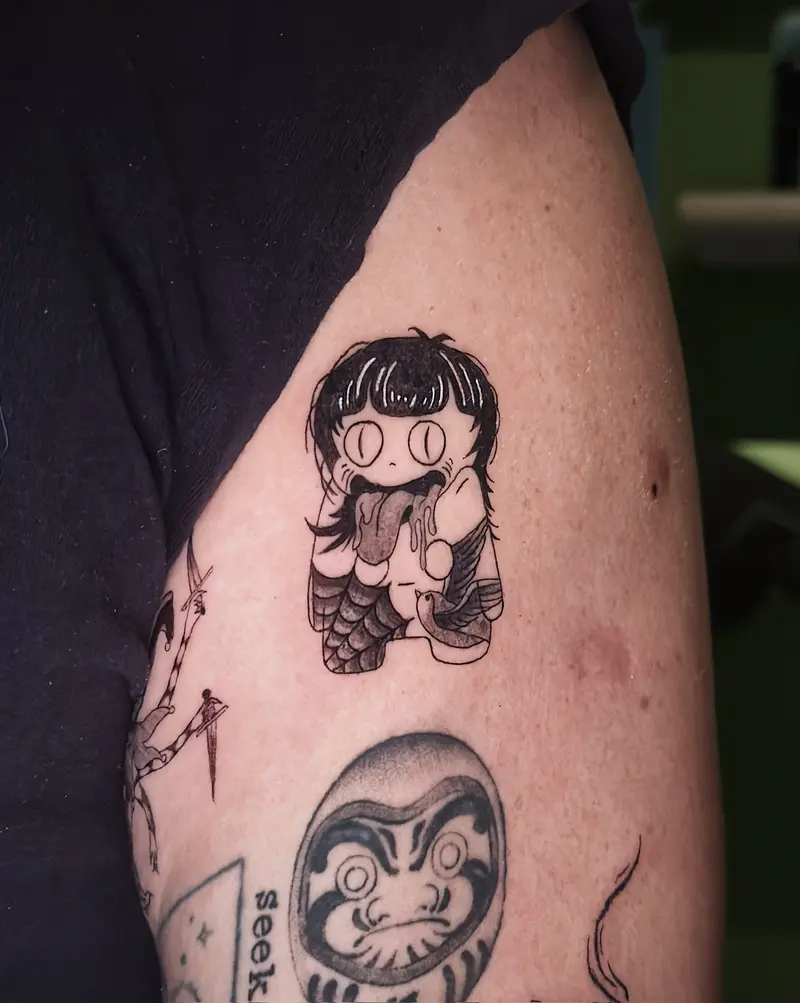Tattoo work: a cartoon character and a daruma in colour, on an arm