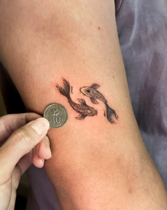 Tattoo work: two small koi beside a coin held against an inner arm
